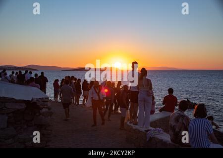 People watch the sunset over the sea at Mykonos. Tourists enjoy a beautiful sunset during the magic hour at Mykonos island in Greece. The Greek island of Myconos is a popular glamorous Mediterranean travel destination for holidays in the Cyclades, Aegean Sea with the iconic whitewashed buildings, the sandy beaches and famous party at the beach bars. The tourism and travel industry had a negative impact in the business and local economy sector due to the Covid-19 Coronavirus pandemic. Mykonos island, Greece on October 10, 2021 (Photo by Nicolas Economou/NurPhoto) Stock Photo