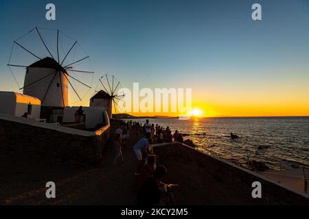 Sunset with people at the windmills in Mykonos. Tourists enjoy a beautiful sunset during the magic hour at Mykonos island in Greece. The Greek island of Myconos is a popular glamorous Mediterranean travel destination for holidays in the Cyclades, Aegean Sea with the iconic whitewashed buildings, the sandy beaches and famous party at the beach bars. The tourism and travel industry had a negative impact in the business and local economy sector due to the Covid-19 Coronavirus pandemic. Mykonos island, Greece on October 10, 2021 (Photo by Nicolas Economou/NurPhoto) Stock Photo