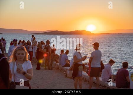 People watch the sunset over the sea at Mykonos. Tourists enjoy a beautiful sunset during the magic hour at Mykonos island in Greece. The Greek island of Myconos is a popular glamorous Mediterranean travel destination for holidays in the Cyclades, Aegean Sea with the iconic whitewashed buildings, the sandy beaches and famous party at the beach bars. The tourism and travel industry had a negative impact in the business and local economy sector due to the Covid-19 Coronavirus pandemic. Mykonos island, Greece on October 10, 2021 (Photo by Nicolas Economou/NurPhoto) Stock Photo