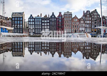 Reflection of the reclining houses. The empty canals of Amsterdam with the tourist sightseeing boats docked. Quiet, almost deserted from local people and tourists streets of Amsterdam during the lockdown in the Dutch capital city with stores and shops appearing with closed with the roller metal shutter down, cafes, bars and restaurants also closed with tables and chairs of the terraces locked. The Netherlands was the first European nation to declare full lockdown to fight the new Omicron variant that surges. After a sudden government order before Christmas, the country closed all the nonessent Stock Photo