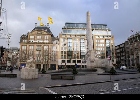 The National Monument and De Bijenkorf department store near Dam Square in Amsterdam during the lockdown. Quiet, almost deserted from local people and tourists streets of Amsterdam during the lockdown in the Dutch capital city with stores and shops appearing with closed with the roller metal shutter down, cafes, bars and restaurants also closed with tables and chairs of the terraces locked. The Netherlands was the first European nation to declare full lockdown to fight the new Omicron variant that surges. After a sudden government order before Christmas, the country closed all the nonessential Stock Photo
