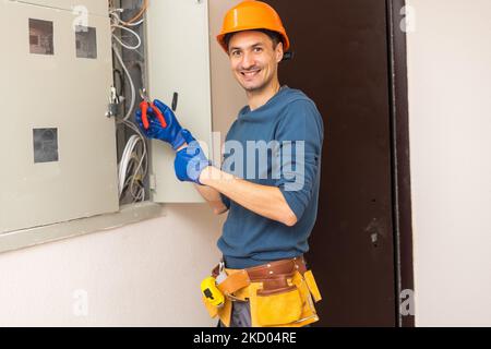 Close up shot of hand of aged electrician repairman in uniform working, fixing, installing ethernet cable in fuse box, holding flashlight and cable Stock Photo