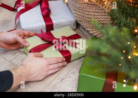 Man putting Christmas gift box under Christmas tree in living room. Stock Photo