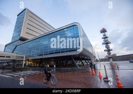 Daily life during the lockdown. A woman as seen on a bike with Amsterdam RAI Exhibition and Convention Centre in the background. Locals and a few tourists at the quiet streets of Amsterdam during the lockdown in the Dutch capital city with stores and shops appearing with closed with the roller metal shutter down, cafes, bars and restaurants also closed with tables and chairs of the terraces locked. The Netherlands was the first European nation to declare full lockdown to fight the new Omicron variant that surges. After a sudden government order before Christmas, the country closed all the none Stock Photo