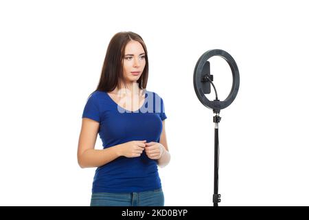 The beautiful girl blogger communicates with the subscribers of her channel using a smartphone and a ring light. Isolated on a white background. Stock Photo