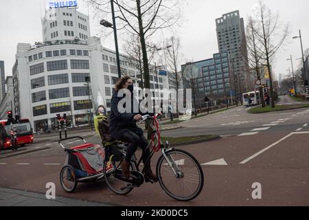 A woman wearing a facemask is cycling on a bike. The Netherlands partly lifts the lockdown measures from 15 of January after the 4-week long lockdown with all the non-essential shops opening with limited working hours, universities, hair dressers and gyms as well, with reduced capacity but cafes, bars and restaurants will still remain closed until 25 January for sure, an action that finds many shop owners against. Daily life in Eindhoven while people walk in the commercial district of the center or wait in line to receive products from stores via click and collect method. Stores and shops appe Stock Photo