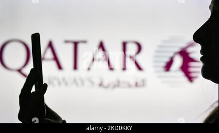 An image of a woman holding a cell phone in front of the Qatar Airways logo displayed on a computer screen. On Tuesday, January 12, 2021, in Edmonton, Alberta, Canada. (Photo by Artur Widak/NurPhoto) Stock Photo