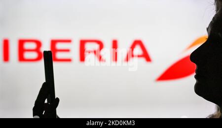 An image of a woman holding a cell phone in front of the Iberia Airlines logo displayed on a computer screen. On Tuesday, January 12, 2021, in Edmonton, Alberta, Canada. (Photo by Artur Widak/NurPhoto) Stock Photo