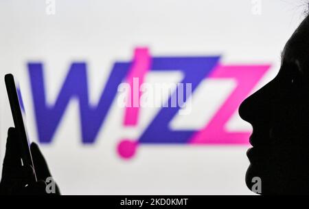 An image of a woman holding a cell phone in front of the Wizz Air logo displayed on a computer screen. On Tuesday, January 12, 2021, in Edmonton, Alberta, Canada. (Photo by Artur Widak/NurPhoto) Stock Photo