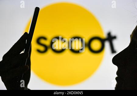 An image of a woman holding a cell phone in front of the Scoot Airline logo displayed on a computer screen. On Tuesday, January 12, 2021, in Edmonton, Alberta, Canada. (Photo by Artur Widak/NurPhoto) Stock Photo