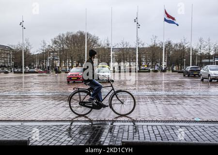 A young person rides a bike with the Dutch flag on a pole during a rainy day. Daily life during the lockdown at the fourth wave of the pandemic. Locals and a few tourists at the quiet streets of Amsterdam during the lockdown in the Dutch capital city with stores and shops appearing with closed with the roller metal shutter down, cafes, bars and restaurants also closed with tables and chairs of the terraces locked. The Netherlands was the first European nation to declare full lockdown to fight the new Omicron variant that surges. After a sudden government order before Christmas, the country clo Stock Photo