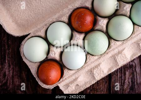 Blue, Green, and Brown Heritage Eggs In an Egg Carton On a Rustic Wood Background: Multicolored eggs in a paper egg carton on a wooden table Stock Photo