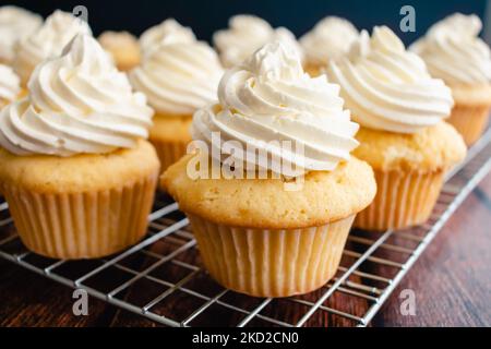 Homemade Vanilla Cupcakes on Wire Cooking Racks: Side view of vanilla cupcakes with vanilla buttercream frosting Stock Photo