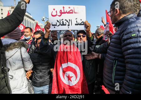 A supporter of the Islamist-inspired party Ennahda wearing the Tunisian flag, shouts slogans as he raises a placard that reads in Arabic “militants against the coup” during a demonstration held at the initiative of “Citizens Against the Coup - the Democratic Initiative” campaign, on Mohamed 5 avenue in the capital Tunis, Tunisia, on February 13, 2022, to protest against the dissolution of the country’s Supreme Judicial Council and called for the independence of the judiciary. Protesters also called for the release of the Vice President of Ennahda party, Noureddine Bhiri who is placed under hou Stock Photo