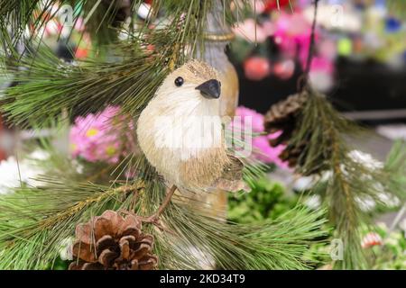 Closeup of Christmas straw bird perched on an artificial tree with pine cones with pink and colorful bokeh background Stock Photo