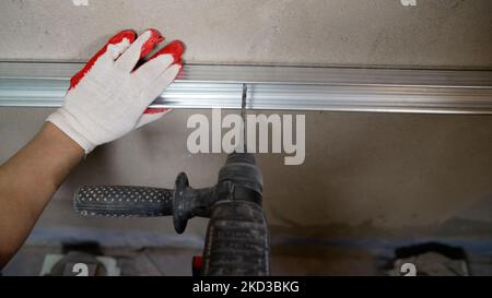 A worker installs a metal shower enclosure profile with a drill. A worker fixes a profile in the bathroom. Stock Photo