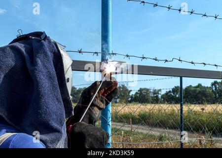 Male welder in brown overalls, protective mask and gloves welds metal pipes to vertical bases for further attachment of metal sheets using electric ar Stock Photo