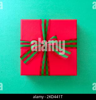 Xmas Anniversary Valentine Day Birthday present. One red gift box wrapped with luxury striped red green ribbon on green background, top view. Stock Photo