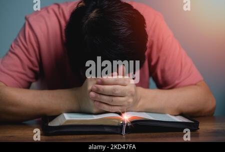 People holding hands head bow down pray to God in the middle book holy bible book with cross necklace front of the holy bible. Stock Photo