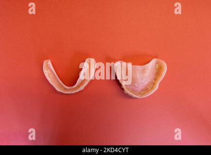 a pair of Dentures (top and bottom) - removable false teeth made of acrylic isolated on a red background - both sets facing down Stock Photo