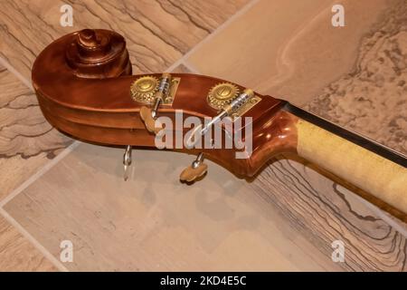The  scroll of a cello composed of nut pegbox and pegs closeup lying on tile floor - selective focus Stock Photo