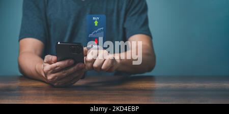 Young man trader trading online on the smartphone apps for buy and sell stock financial market with chart. Stock Photo