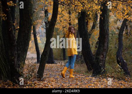 girl in a yellow raincoat and yellow rubber boots walks in the park. autumn in the city Stock Photo