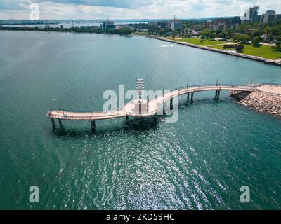 The Brant Street Pier on the rocky shore of Lake Ontario with the cityscape in the distance Stock Photo