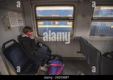 A young woman talking to the phone while she sits in the train with her luggage. Ukrainian people, mostly women, mothers with children or elderly, the war refugees as seen boarding the train railroad car, they get in fast after waiting underground at Lviv railway station passageway the train to arrive and board on the carriages quickly as the station is considered as a military target. The train is going to cross the Polish Ukrainian borders and travel further to Poland and other European Countries. On March 15 the sirens for air raid sounded two times, one in the morning and one in the evenin Stock Photo