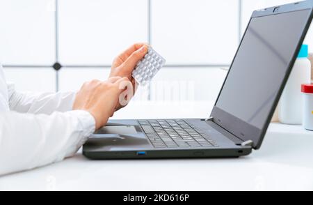 young woman holds a package of medical pills in her hands and reads instructions for use on a computer Stock Photo