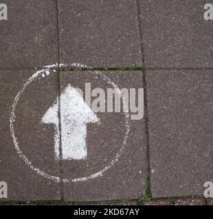 dirty white arrow in a circle of grey paving blocks on the pavement Stock Photo