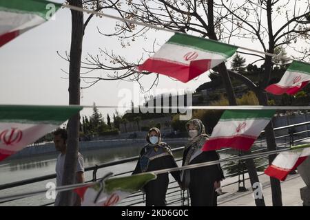 Two Iranian women walk past Iran flags in the Art Museum Garden in northern Tehran during a ceremony to mark Iran’s Islamic Republic National day on April 1, 2022. Iranian people voted yes in a referendum for the Islamic Republic regime forty three years ago. (Photo by Morteza Nikoubazl/NurPhoto) Stock Photo