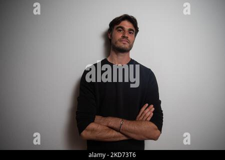 Young Caucasian man with crossed arms resting on wall looks straight ahead of camera. Stock Photo