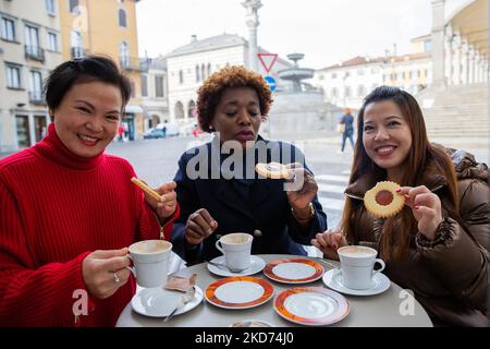 Three happy multiracial women seated at bar having breakfast. Cappuccino concept. Stock Photo