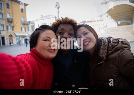 Three toothy smiling diverse friends take selfie during their walk at the city center. Stock Photo