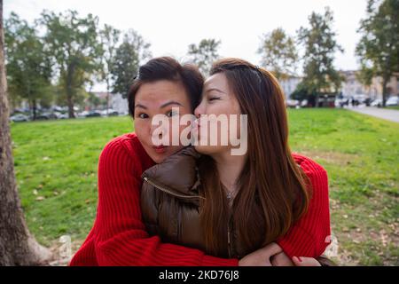 Two Chinese female friends hugging in the park. One kisses the other on the cheek. Stock Photo