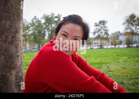 Attractive smiling middle aged chinese woman sitting on the grass at the park. Stock Photo