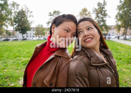 Two Chinese friends at the park back to back look into each other's eyes. Stock Photo