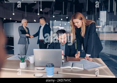 Two smiling coworkers working together analyzing the charts in office on colleagues background Stock Photo