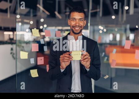 African Businessman showing sticky notes with motivational phrases while standing in office Stock Photo