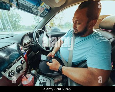 A bearded man using phone while driving a car. Texting while driving. Stock Photo