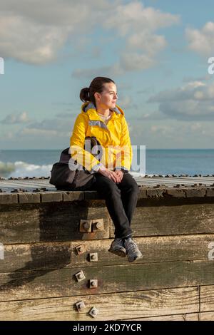 sad woman sitting alone by the sea, wearing a yellow coat. Stock Photo