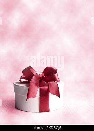 Round gift boxe with red ribbon and bow on pink background. Stock Photo