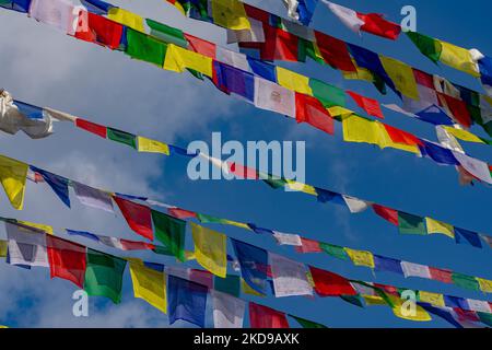 A blue cloudy sky with colorful Dar Cho prayer flags hanging on the ropes in the foreground Stock Photo