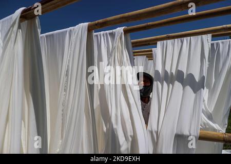 A worker hangs a cloth to dry out on the sun beside homes surrounded by rising sea levels at low-lying Jeruk Sari neighborhood in coastal Pekalongan, Central Java, Indonesia, June 5, 2021. An area in which almost every available space is used for batik production, with a high level of poverty, vulnerable to both rising sea levels and high river peak flows. They hangs and washes at a polluted river for process traditional Javanese textile called Batik. Batik is a traditional Indonesian method of using wax to resist water-based dyes to depict patterns and drawings on fabric. At the heart of the  Stock Photo