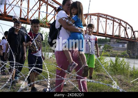 Migrants, most with children follow a path along the concertina wire where ultimatley they will placed under guard by Border Patrol after having crossed the Rio Grande on May 27 2022 in Eagle Pass Texas, USA. Title 42, the Trump era mandate which was set to prevent migrants from entering the US, was to expire on May 23 but was blocked by a lawsuit filed by several states citing that the move to strike down the law “failed to meet standards set by the Administrative Procedure Act” and that there is no permanent solution to handling the inevitable surge in immigration. Opponents to upholding of  Stock Photo