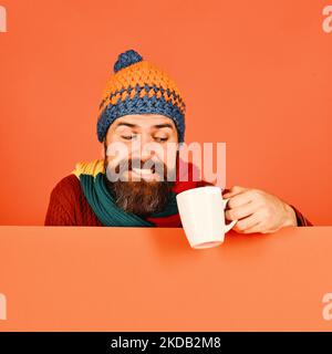 Man in warm hat holds white cup on orange background Stock Photo