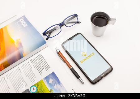 In this photo illustration a Binance logo seen displayed on a smartphone screen on a desk next to a cafe, a pen, glasses and a magazine in Athens, Greece on May 31, 2022. (Photo illustration by Nikolas Kokovlis/NurPhoto) Stock Photo