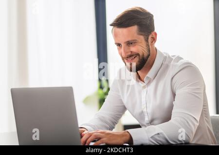Bearded man entrepreneur in white shirt typing on keyboard, smiling Stock Photo