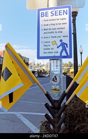 A sign states to 'Be Seen' as pedestrians are asked to carry a yellow flag while crossing a street in downtown Pagosa Springs, Colorado. Stock Photo